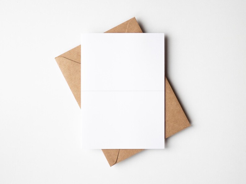 May include: A blank white folded card rests on top of a brown paper envelope. The card is centered, with the envelope's corner visible. The background is a plain white surface, creating a minimalist aesthetic.