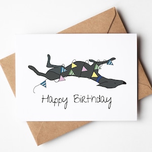May include: A white card with a black and grey illustration of a dog with colourful party flags wrapped around it. The text "Happy Birthday" is written below the dog.