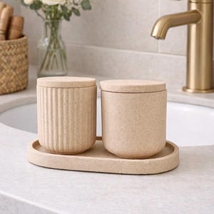 May include: Two cylindrical beige containers with matching lids, one featuring a vertical ribbed texture and the other a smooth speckled finish, both resting on an oval tray of the same light tan material and speckled composition.