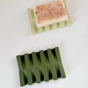 Puede incluir: Una taza de cerámica blanca con un asa negra y el texto "But First, Coffee" en negrita negra. La taza se encuentra sobre un fondo borroso, sugiriendo un ambiente acogedor.