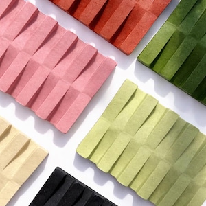 May include: An overhead shot showcases six rectangular, textured objects in various colors: red, pink, green, yellow, light green, and black. Each object has a pleated design, creating a repeating pattern of angled lines.