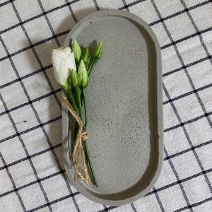 May include: A gray oval concrete tray with a bouquet of white flowers and green stems.