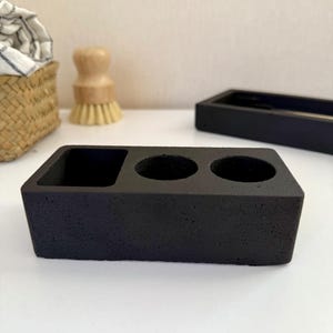 May include: Black ceramic dish with three round indentations for holding small items, such as brushes or tools.