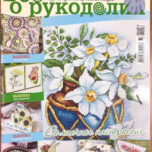 Puede incluir: Una portada de revista con diseños de punto de cruz. La portada muestra un arreglo floral en un jarrón azul, con el texto "Revista para gente creativa". Imágenes adicionales muestran varios proyectos de bordado, incluyendo una almohada, diseños florales y manualidades temáticas de Pascua.