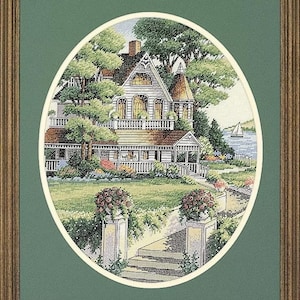 Peut inclure: Un motif de point de croix représentant une maison blanche avec un porche et un jardin. La maison est entourée d'arbres et de buissons verts. Il y a un petit bateau dans l'eau à l'arrière-plan.