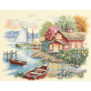 Può includere: Uno schema di punto croce che raffigura un cottage rosso con una staccionata bianca, incastonato su una costa rocciosa con una barca a vela e due barche a remi rosse nell'acqua. Alberi verdi lussureggianti e fiori colorati circondano il cottage.