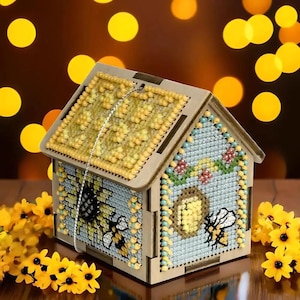 Peut inclure: Une boîte en bois en forme de maison avec un motif d'abeille et de nid d'abeille. La boîte est décorée de broderie au point de croix et possède un couvercle en plastique transparent.