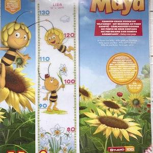 Puede incluir: Un kit de punto de cruz contado con el personaje Maya la Abeja. El kit incluye una tabla de altura con Maya y flores, con medidas de hasta 130 cm. El embalaje incluye el texto "Maya" y "Studio 100".