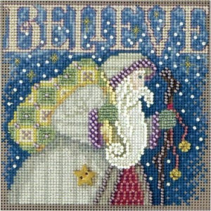 Può includere: Un ricamo a punto croce su tessuto a griglia raffigurante una figura barbuta con tunica e cappello bianchi, che trasporta un sacco a motivi verdi e gialli. La parola BELIEVE è ricamata in grandi lettere sopra, con un bottone a stella dorato.