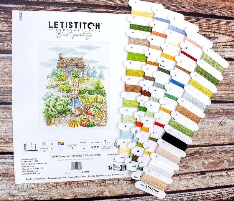 May include: A cross stitch kit featuring a colorful illustration of a rabbit in a garden with a house in the background. The kit includes a variety of DMC threads and a printed fabric. The kit is titled "Summer Harvest" and is by Letistitch.