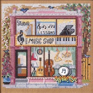 May include: A cross-stitch embroidery depicting a two-story music shop with a pink facade. The storefront window displays a double bass, saxophone, and drum. Text reads STUDIO, LESSONS, and MUSIC SHOP. Blue birds and floral accents surround the building.