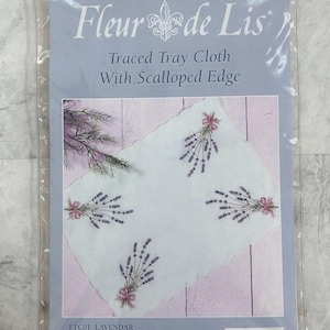 May include: A packaged lavender-themed traced tray cloth with a scalloped edge. The cloth features embroidered lavender sprigs with pink bows. The package reads "Fleur de Lis" and "Traced Tray Cloth With Scalloped Edge". The cloth measures 19¾" x 13¾".