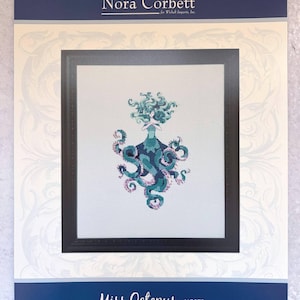 May include: A framed cross-stitch design featuring "Miss Octopus" by Nora Corbett. The artwork depicts an octopus-like figure in shades of teal, blue, and purple. The design is set against a white background within a black frame, with the artist's name at the top.