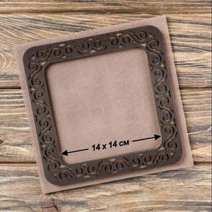 May include: A brown wooden frame with a decorative design, measuring 14 inches by 14 inches. The frame is on a beige fabric background.