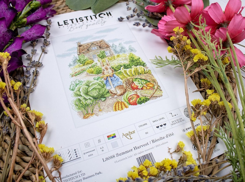 May include: A cross-stitch pattern featuring a rabbit holding a basket of vegetables in front of a cottage. The pattern is titled "L8088 Summer Harvest / R&eacute;colte d'&eacute;t&eacute;" and is by Anchor.
