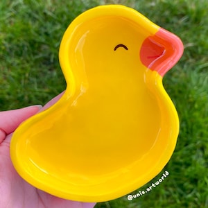 Peut inclure: Un plat en céramique jaune en forme de caneton avec un bec rouge et les yeux fermés. Le plat est parfait pour contenir de petits objets comme des bijoux ou des clés.