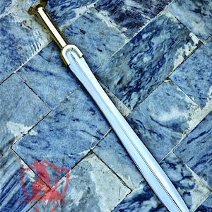 May include: A long, silver sword with a gold-colored handle and guard. The blade is straight and tapers to a point. The sword rests on a blue and gray tiled surface. The handle has a rounded pommel.
