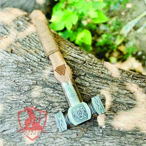 May include: A detailed image of a hammer with a wooden handle wrapped in twine. The hammerhead is a light green colour with intricate Celtic knot designs. The hammer is resting on a textured wooden surface.
