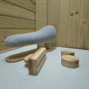 May include: A light gray fabric-covered tailor's ham with a light-colored wooden base, accompanied by a rectangular wooden pressing block and two small, round wooden pressing tools, all designed for garment sewing and ironing tasks.