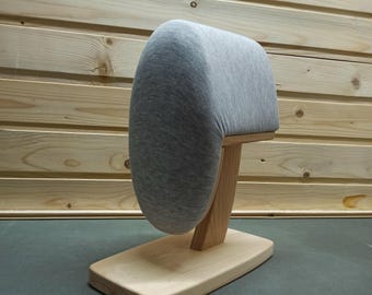 May include: A tailor's ham pressing tool featuring a rounded, heather gray fabric-covered cushion mounted on a light-colored wooden stand with a rectangular base. The cushion is designed for pressing curved seams and shaping garments during sewing.
