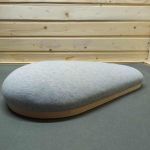 May include: A gray fabric cushion with a wooden base. The cushion is shaped like a teardrop and has a soft, plush texture.