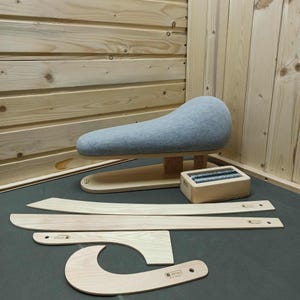 May include: A gray padded ironing board with a wooden base, accompanied by several wooden tools and a small wooden box with metal coils. The tools include curved and straight pieces, likely for garment shaping and pressing.