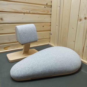 May include: Two gray fabric cushions with wooden bases. The larger cushion is shaped like a teardrop and the smaller cushion is rectangular. Both cushions are on a wooden surface.