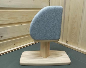May include: A light gray fabric-covered head-shaped display form mounted on a light-colored wooden pedestal base. The display features a curved, rounded top section supported by a vertical wooden post attached to a flat, rectangular wooden stand.