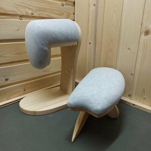 Könnte beinhalten: Zwei Holz-Schneiderpuppen mit grauer Stoffpolsterung. Eine ist eine große Form mit rundem Sockel und gebogenem Hals. Die andere ist ein kleiner Hocker mit drei Beinen und gepolsterter Sitzfläche.