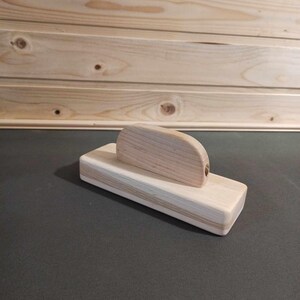 May include: A wooden block with a curved top, made of light wood. The block is sitting on a dark surface.