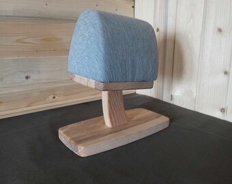 May include: A wooden headrest stand with a gray fabric padded top. The stand has a simple design with a single post and a wide base.