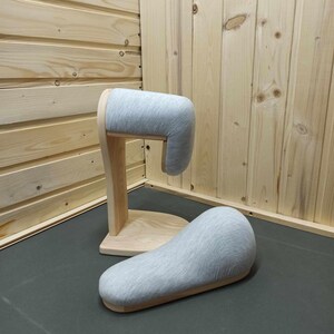 Può includere: Un poggiatesta in legno con un cuscino in tessuto grigio. Il poggiatesta è progettato per sostenere la testa e il collo mentre si è seduti o sdraiati.