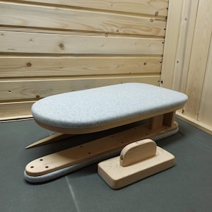 Könnte beinhalten: Ein Bügelbrett aus Holz mit einer hellgrau gepolsterten Oberfläche, ein Bügelbrett für Ärmel und ein Bügelholz. Das Bügelbrett hat ein geschwungenes Design und ist aus hellem Holz gefertigt.