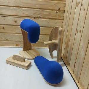 Può includere: Un set di quattro strumenti da sartoria in legno che include due cuscini da stiro rivestiti in tessuto blu, un blocco da stiro rettangolare in legno con manico e un supporto verticale in legno con braccio di supporto curvo.