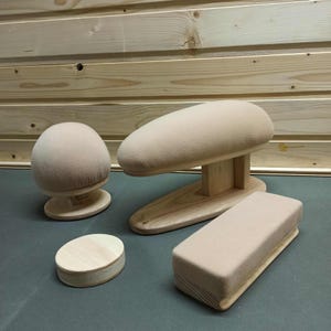 May include: A collection of wooden dressmaking tools, including a rounded head form, a long oval form, a small oval form, and a rectangular form, all covered in a light beige fabric. The wooden bases are unfinished.