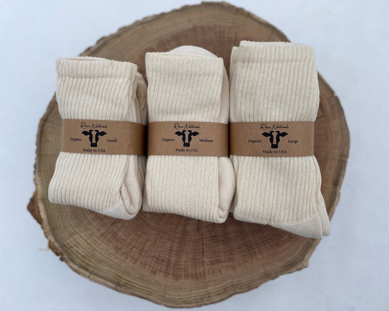 Puede incluir: Tres pares de calcetines de algod&oacute;n org&aacute;nico en diferentes tama&ntilde;os: peque&ntilde;o, mediano y grande. Los calcetines son de color crema natural y est&aacute;n doblados cuidadosamente sobre una superficie de madera. Cada par tiene una etiqueta marr&oacute;n con el texto "Run Naturals" y el tama&ntilde;o de los calcetines.