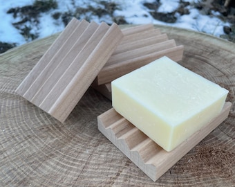 Könnte beinhalten: Zwei Seifenablagen aus Holz mit einem weißen Stück Seife darauf. Die Seifenablagen sind aus hellbraunem Holz und haben ein gerilltes Design.