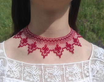 May include: A red beaded choker necklace with a delicate floral design. The necklace is worn by a person with long dark hair and a white lace top.