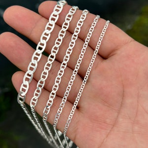 May include: Five silver mariner chain necklaces of varying widths, displayed on a hand.