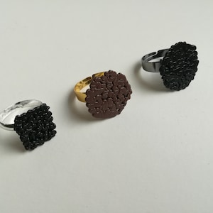 Op de afbeelding: Drie verstelbare ringen met zwarte, bruine en zilveren banden. Elke ring heeft een uniek, getextureerd ontwerp.
