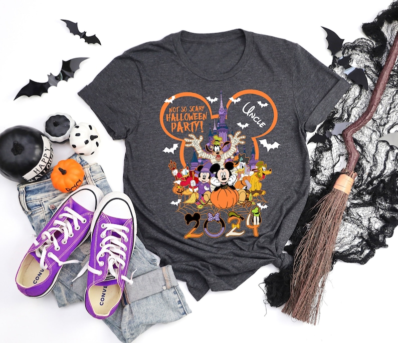 May include: Dark gray t-shirt with a colorful Halloween-themed graphic featuring Disney characters, the text "Not So Scary Halloween Party!" and "Uncle". The shirt is styled with purple Converse sneakers, jeans, and Halloween decorations.