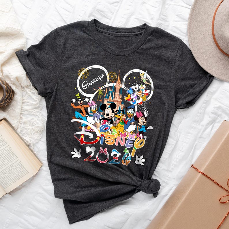 May include: Dark gray t-shirt featuring a colorful Disney graphic. The design includes Mickey Mouse, Donald Duck, and other characters, with the text "Grandpa Disney 2020". The shirt is knotted at the waist.