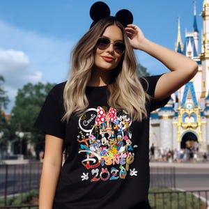 May include: Black t-shirt featuring a colorful Disney graphic with Mickey Mouse, Minnie Mouse, and other characters. The shirt includes the text "Cousin Disney 2020" and is set against a theme park backdrop.