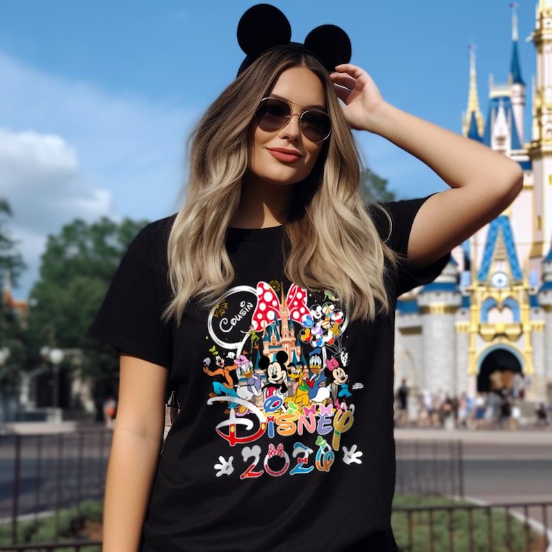 May include: Black t-shirt featuring a colorful Disney graphic with Mickey Mouse, Minnie Mouse, and other characters. The shirt includes the text "Cousin Disney 2020" and is set against a theme park backdrop.