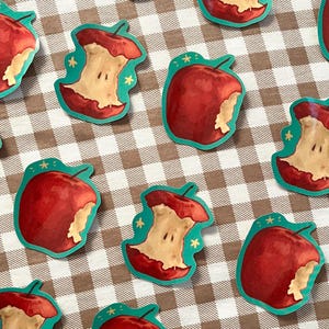 May include: A set of ten teal and red apple stickers with a bite taken out of them. The stickers have a white background with a few small stars.