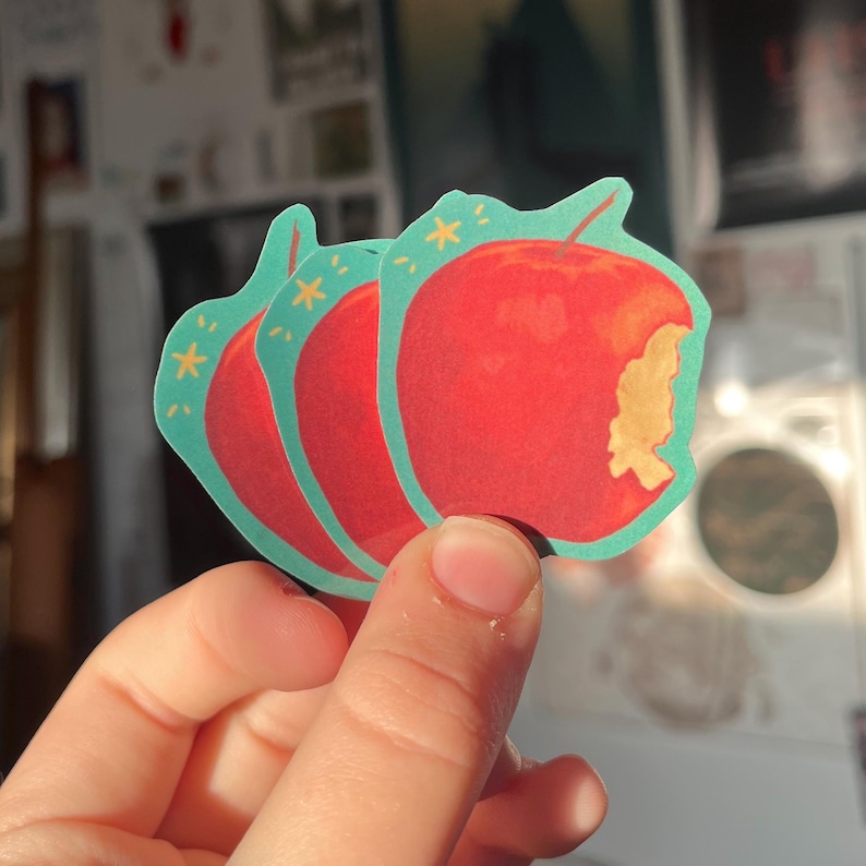 May include: Three red apple stickers with a bite taken out of one. The stickers have a teal border and yellow stars.