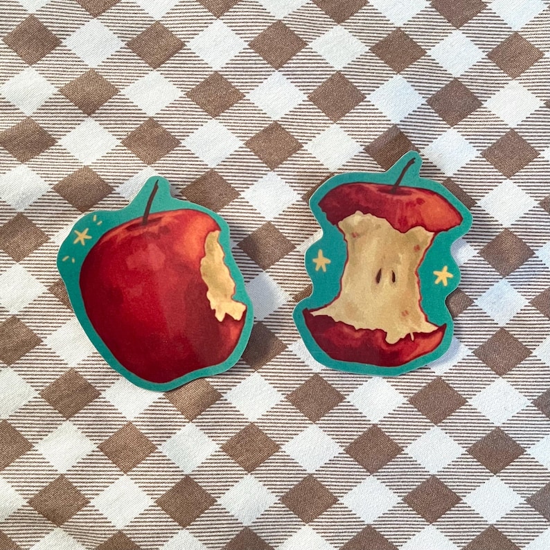 May include: Two red apple stickers, one whole and one with a bite taken out. The stickers are on a brown and white checkered background.