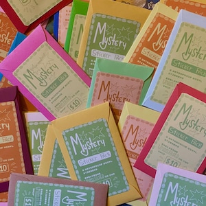 May include: A collection of colourful paper envelopes containing mystery sticker packs. Each envelope features a label with the text Mystery Sticker Pack, 5 waterproof vinyl stickers, and a $10 price tag, surrounded by a decorative hand-drawn border.