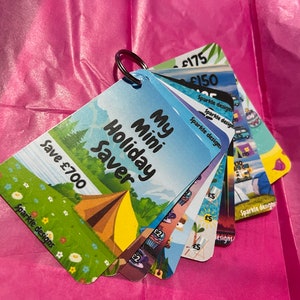 May include: A set of colourful cards with a camping theme. The cards are labelled with different amounts of money, such as "£150" and "£175". The largest card has a blue sky background with a tent and the text "My Mini Holiday Saver" and "Save £700".