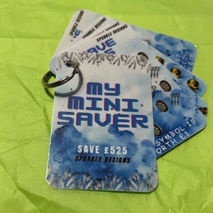 May include: A blue and white card with the text "My Mini Saver" and "Save £525 Sparkle Designs". The card is attached to a silver key ring.
